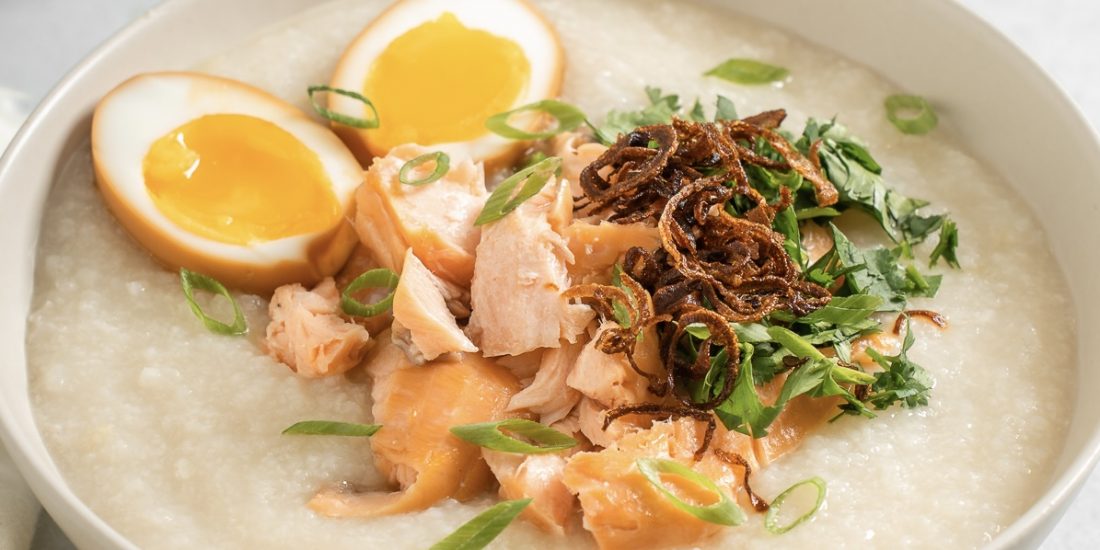 Smoked salmon congee topped with crispy shallots, herbs, and soy eggs.