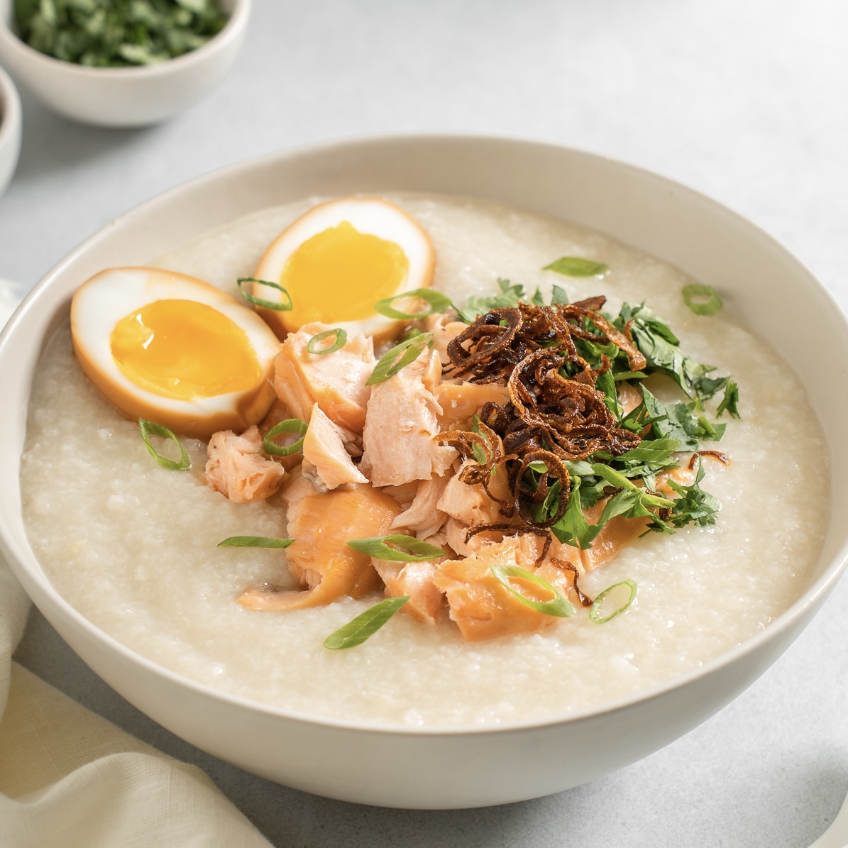 Smoked salmon congee topped with crispy shallots, herbs, and soy eggs.